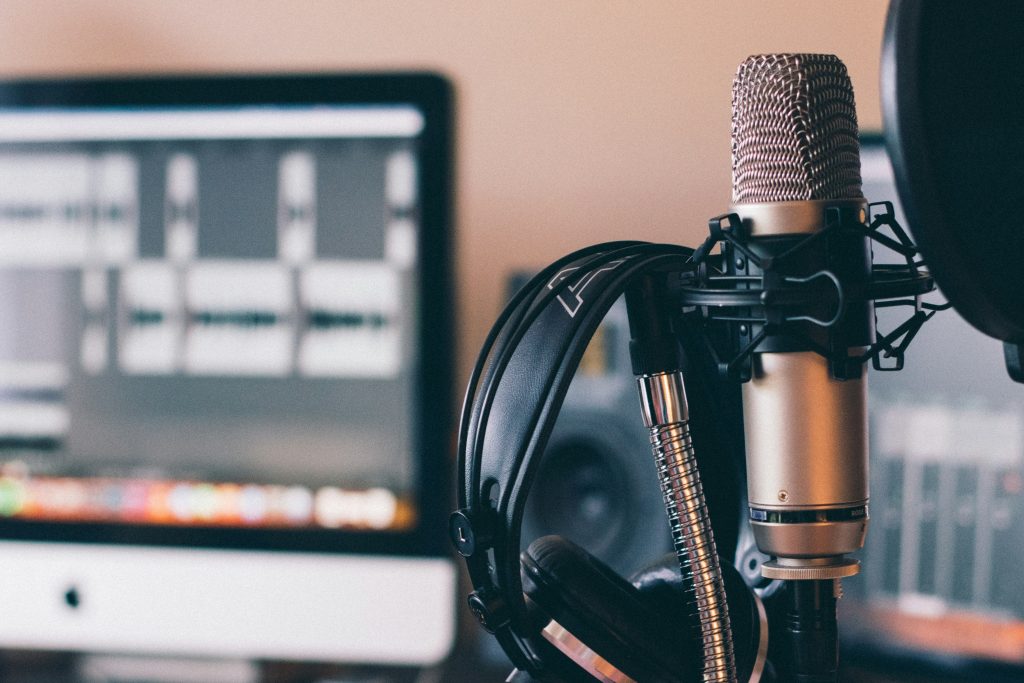 Image of a microphone in front of a computer monitor with the DAW (digital audio workstation) on the screen.
